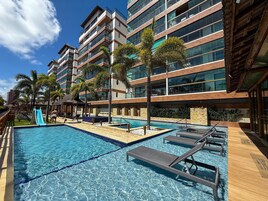 Área de piscina de hotel com piscina azul límpida, espreguiçadeiras e palmeiras.