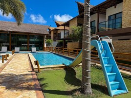 Piscina com escorregador, espreguiçadeiras e deck de madeira.