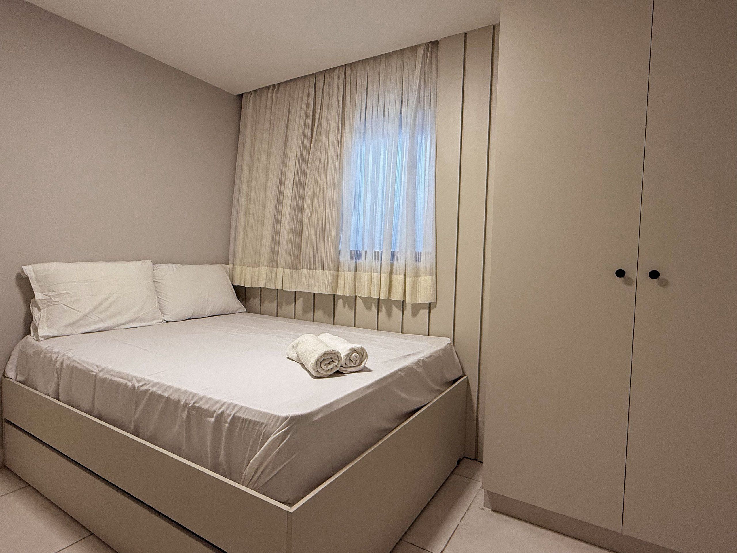 Un dormitorio con cama, ventana con cortinas translúcidas y armario.