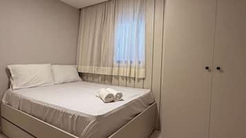 Un dormitorio con cama, ventana con cortinas translúcidas y armario.
