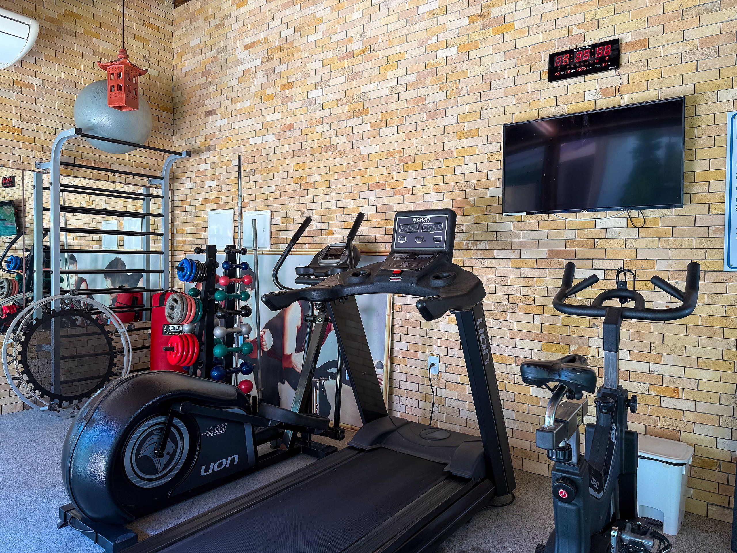 Un gimnasio con equipo de ejercicio, un reloj digital y un televisor en la pared.