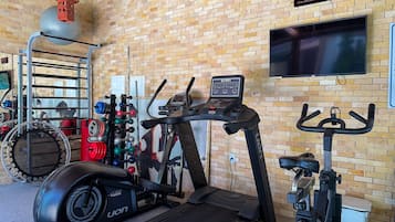 Un gimnasio con equipo de ejercicio, un reloj digital y un televisor en la pared.