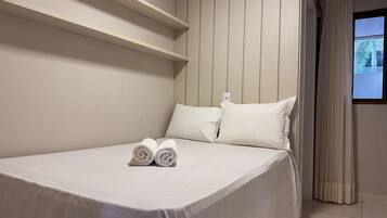 Habitación de hotel con cama, almohadas, una toalla doblada y un ventanal con cortinas.