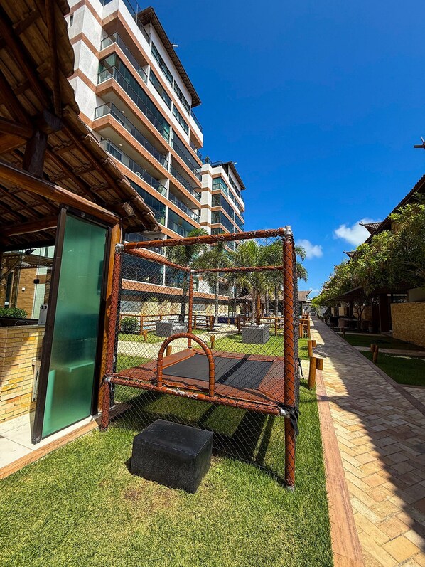 Un espacio exterior cercado con un banco, una mesa pequeña y un sendero que lleva a un edificio con varios balcones.