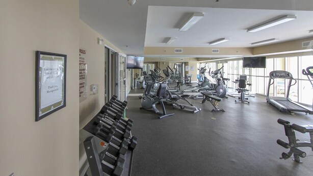 Une salle de sport équipée de matériel d’exercice, d’un tapis de course et d’un mur recouvert de miroirs.