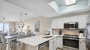 Une cuisine moderne avec des meubles blancs, des appareils en acier inoxydable et un îlot central doté d’un évier.