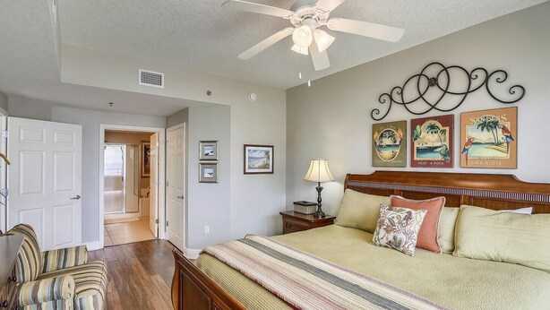 A bedroom with a bed, a nightstand, a lamp, a ceiling fan, and wall art. - Ariel Dunes I 610- Emerald Eden (Miramar Beach)