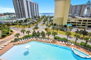 A resort with a swimming pool, palm trees, and high-rise buildings in the background. - Ariel Dunes I 610- Emerald Eden (Miramar Beach)