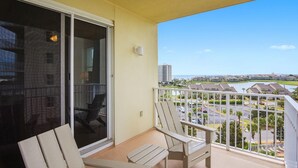 A balcony with two chairs, a sliding glass door, and a view of a residential area with buildings and a body of water. - Ariel Dunes I 610- Emerald Eden (Miramar Beach)