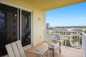 A balcony with two chairs, a sliding glass door, and a view of a residential area with buildings and a body of water. - Ariel Dunes I 610- Emerald Eden (Miramar Beach)