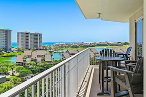 A balcony with a table and chairs, overlooking a resort area with buildings and a pool. - Ariel Dunes I 610- Emerald Eden (Miramar Beach)