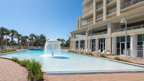 A swimming pool with a water fountain, surrounded by lounge chairs and a building with balconies. - Ariel Dunes I 610- Emerald Eden (Miramar Beach)
