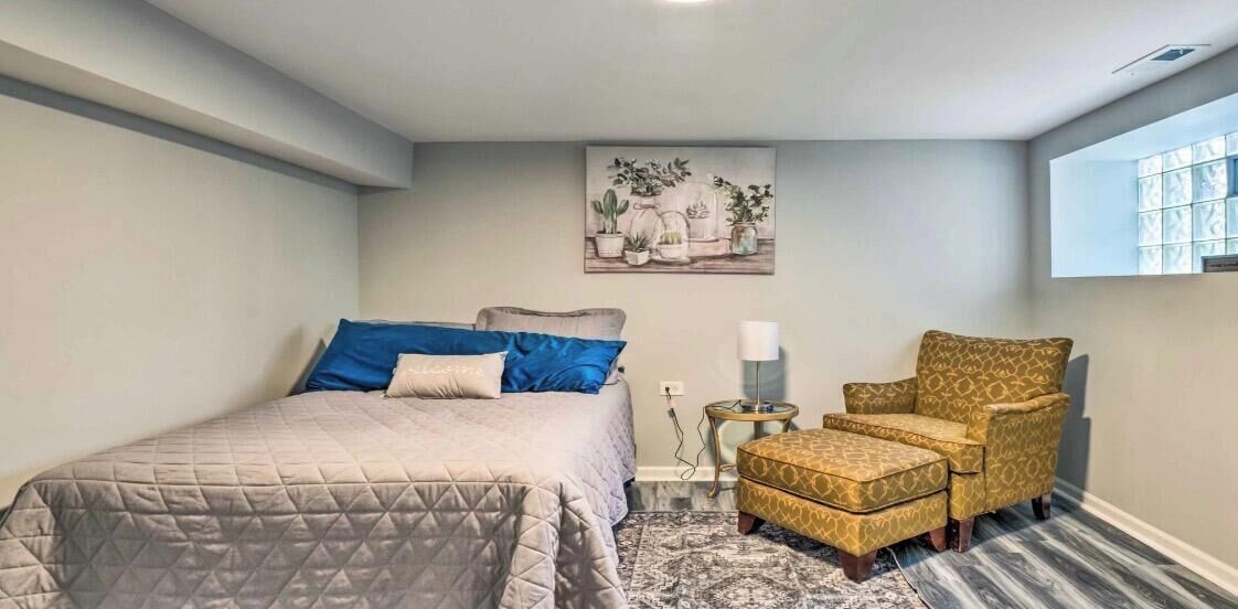 A bedroom with a bed, a chair, a small table, and a window.