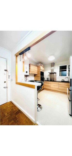 A modern kitchen with wooden cabinets, a black countertop, and pendant lighting. - Elegant 2BR Apartment with Balcony & Free Parking (Ivry-sur-Seine)