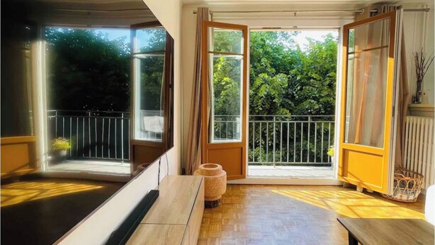 Ruime kamer met een grote schuifglazen deur naar een balkon, een houten vloer en een bankje.