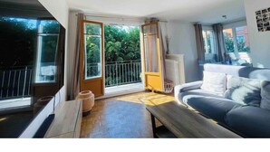 Een ruime kamer met een groot raam, een bank, een houten bankje en een radiator.
