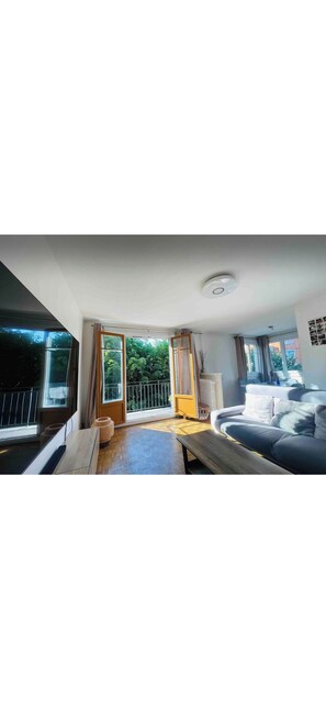 A spacious room with a large window, a sofa, a wooden bench, and a radiator. - Elegant 2BR Apartment with Balcony & Free Parking (Ivry-sur-Seine)