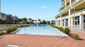 A swimming pool with lounge chairs, a white umbrella, and a building with balconies. - Ariel Dunes I 801- Morning Raes (Miramar Beach)