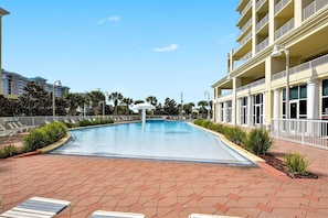A swimming pool with lounge chairs, a white umbrella, and a building with balconies. - Ariel Dunes I 801- Morning Raes (Miramar Beach)