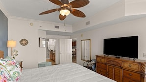 A bedroom with a bed, a ceiling fan, a dresser, a television, and a bathroom visible through an open door. - Ariel Dunes I 801- Morning Raes (Miramar Beach)