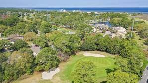 An aerial view of a golf course with sand bunkers, trees, and residential buildings in the background. - Beach and Bay for Days @ Heron Walk (Miramar Beach)