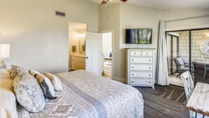A bedroom with a bed, dresser, TV, and a balcony with seating. - Beach and Bay for Days @ Heron Walk (Miramar Beach)