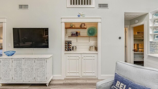 A living room with a TV, decorative items, and a built-in cabinet. - Beach and Bay for Days @ Heron Walk (Miramar Beach)