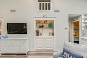 A living room with a TV, decorative items, and a built-in cabinet. - Beach and Bay for Days @ Heron Walk (Miramar Beach)