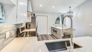 A modern kitchen with a built-in stove, a coffee maker, and a sink with a high-arc faucet. - Beach and Bay for Days @ Heron Walk (Miramar Beach)
