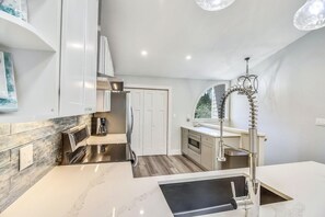 A modern kitchen with a built-in stove, a coffee maker, and a sink with a high-arc faucet. - Beach and Bay for Days @ Heron Walk (Miramar Beach)