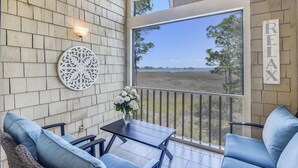 A covered patio with a table and chairs, a decorative wall piece, and a view of a natural landscape. - Beach and Bay for Days @ Heron Walk (Miramar Beach)