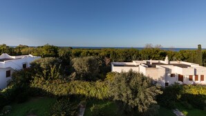 Edifici blanc amb diverses finestres i teulada plana, envoltat de verdura i arbres, sota un cel clar.