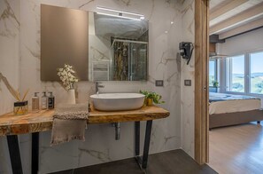 Un baño moderno con pared de mármol, tocador de madera, espejo grande, lavabo blanco y ducha.
