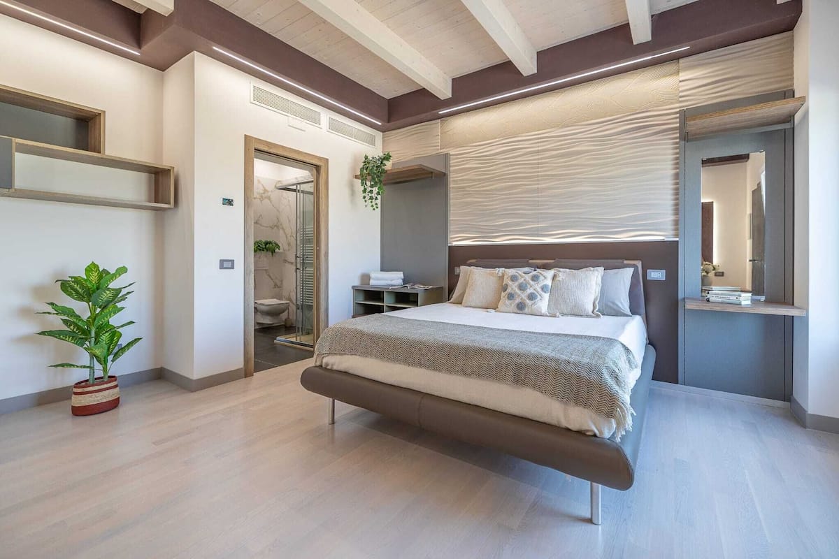 A modern bedroom with a bed, a potted plant, a bathroom, and a mirror.