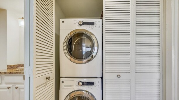 Una lavanderia con due lavatrici a carica frontale impilate e una porta bianca con listelli orizzontali.