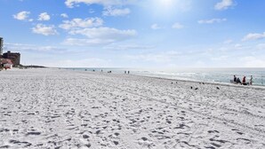Ampia spiaggia sabbiosa con impronte, cielo sereno e alcune persone.