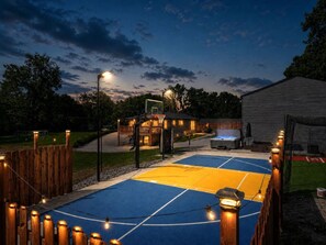Un terrain de basket en plein air, entouré d’une clôture en bois, avec un panier de basket et un bâtiment visible à l’arrière-plan.
