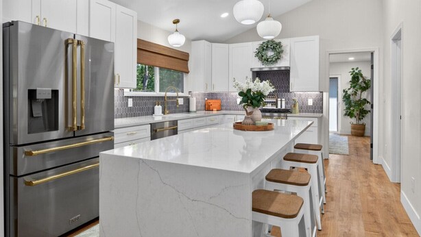 A modern kitchen with white cabinetry, stainless steel appliances, a large island with stools, pendant lighting, and a view of the outdoors. - The Stadium by Mercer Stays | Private 2.2Acre Sports Estate for Teams & Families (Saint Charles)