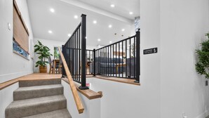 A staircase with wooden steps and black railings, leading to a room with a gray sofa and a plant. - The Stadium by Mercer Stays | Private 2.2Acre Sports Estate for Teams & Families (Saint Charles)