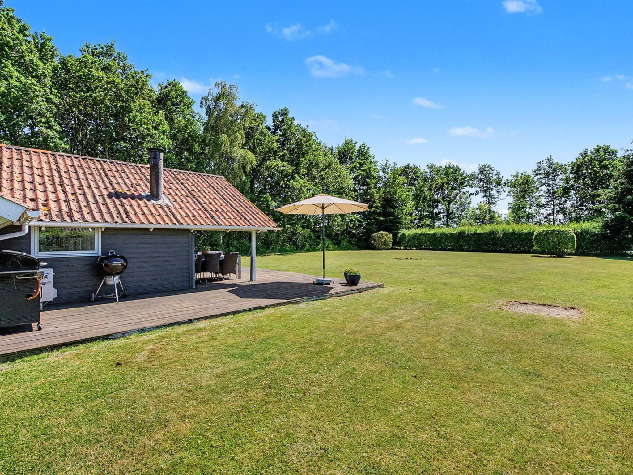 A house with a tiled roof, a barbecue area, and a covered patio with a table and chairs.
