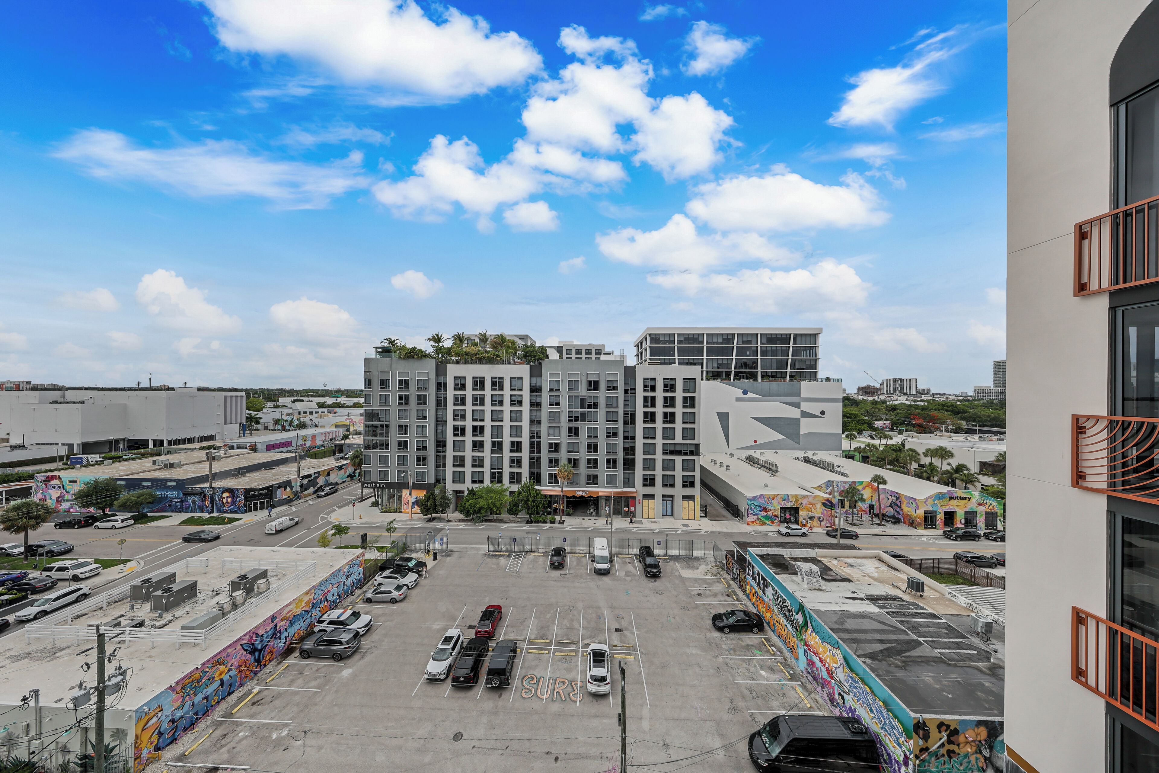 A multi-story parking garage with a mural on the side, surrounded by buildings and a clear sky.