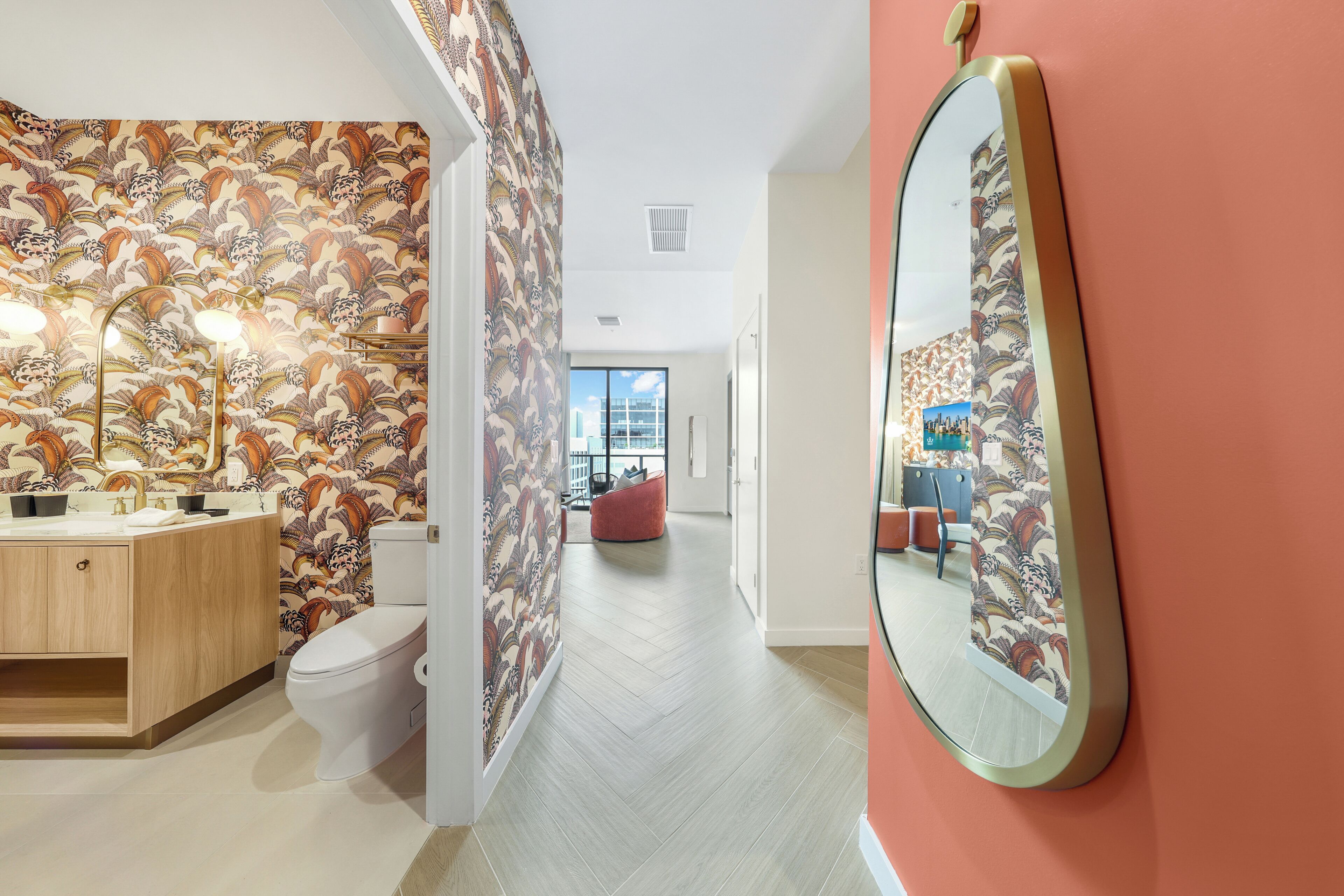 A modern bathroom with a patterned wallpaper, a wooden vanity, a white toilet, and a large mirror.