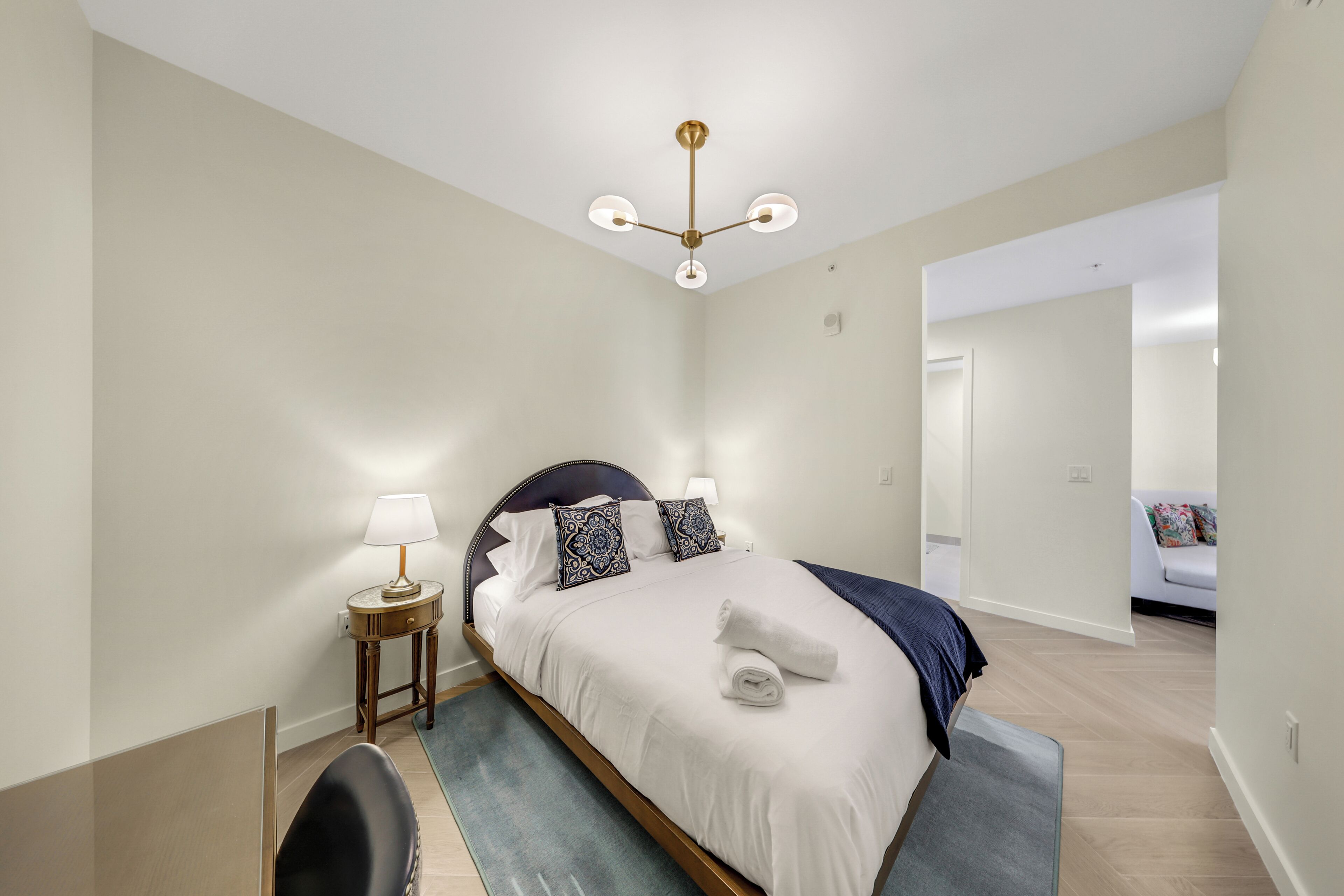 A bedroom with a bed, bedside tables, a lamp, a ceiling fan, and a door leading to another room.