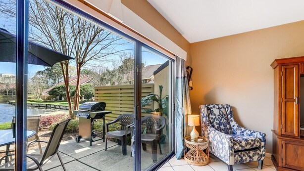 Una habitación con puerta corrediza de vidrio que da a un patio con mobiliario exterior y una parrilla.