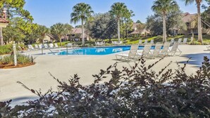 Una piscina con sillones de descanso, rodeada de palmeras y casas.