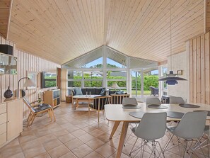 Ein geräumiges Zimmer mit hohen Decken, Holzwänden, einem großen Fenster und einem Essbereich mit modernen Stühlen und Tischen.