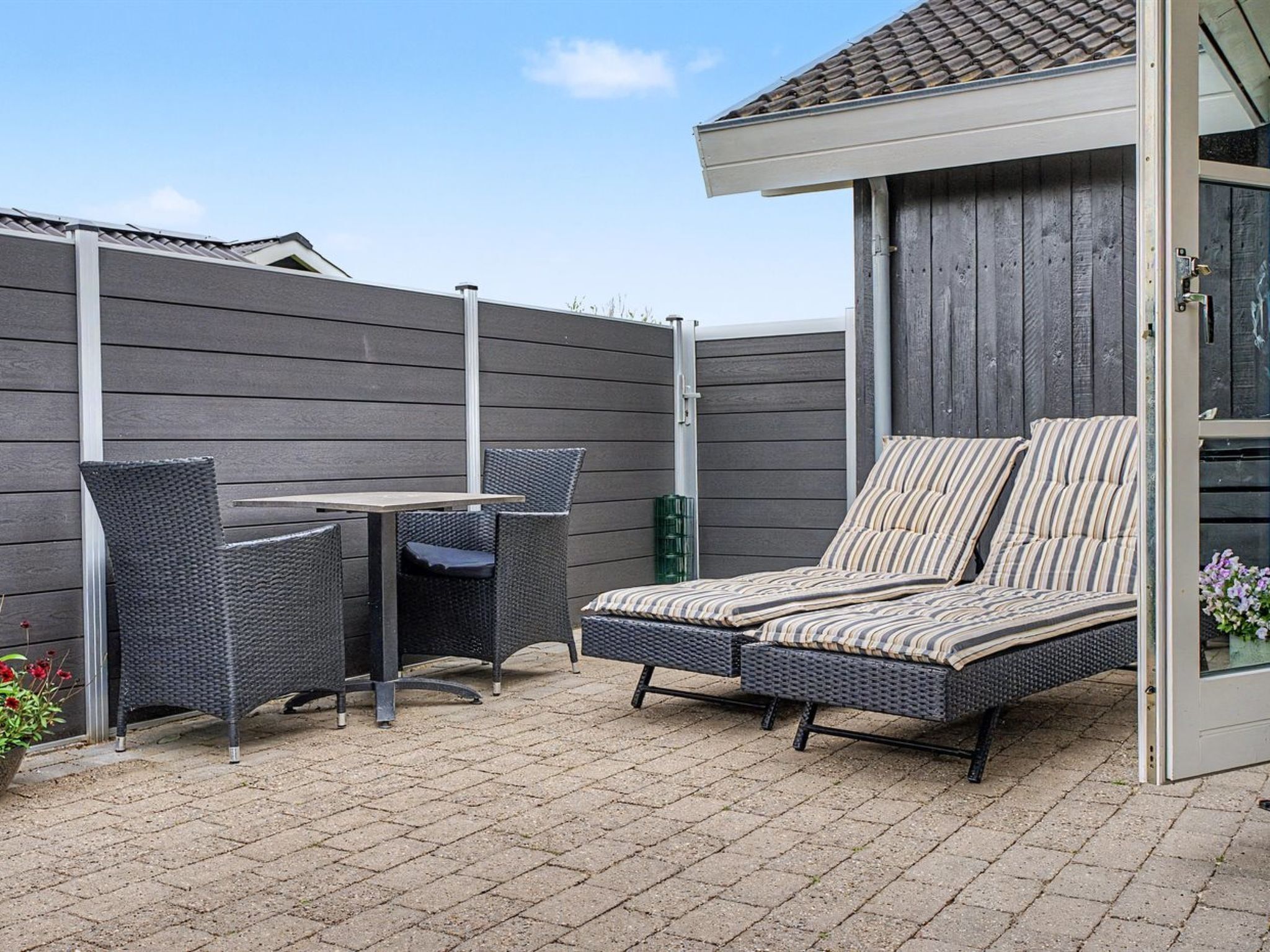 A patio with a table and chairs, a cushioned lounge area, and a wooden fence.