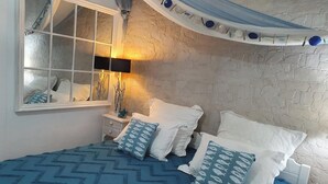 Un dormitorio con cama, mesita de noche, lámpara, espejo y ventana con cortinas.