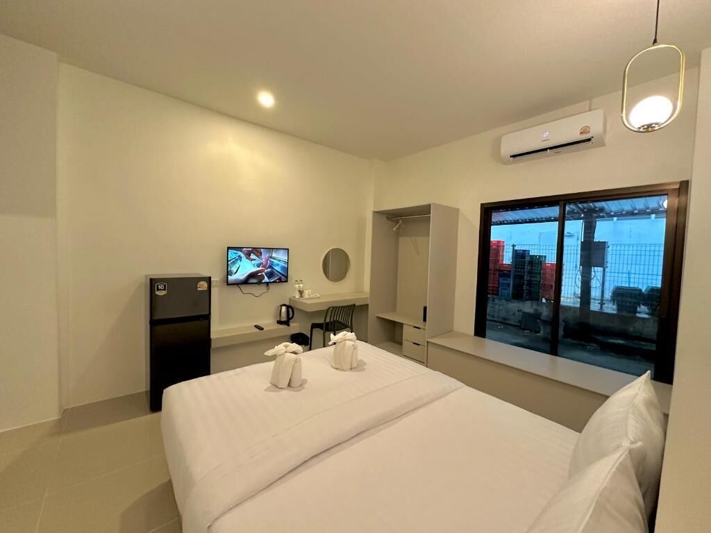 A hotel room with a bed, a TV, a refrigerator, a window with a view, and an air conditioning unit.