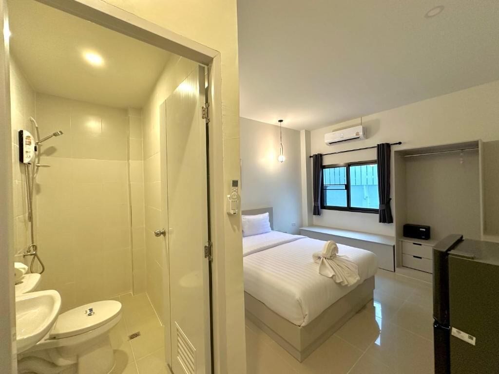 A hotel room with a shower, toilet, bed, window, and a TV.